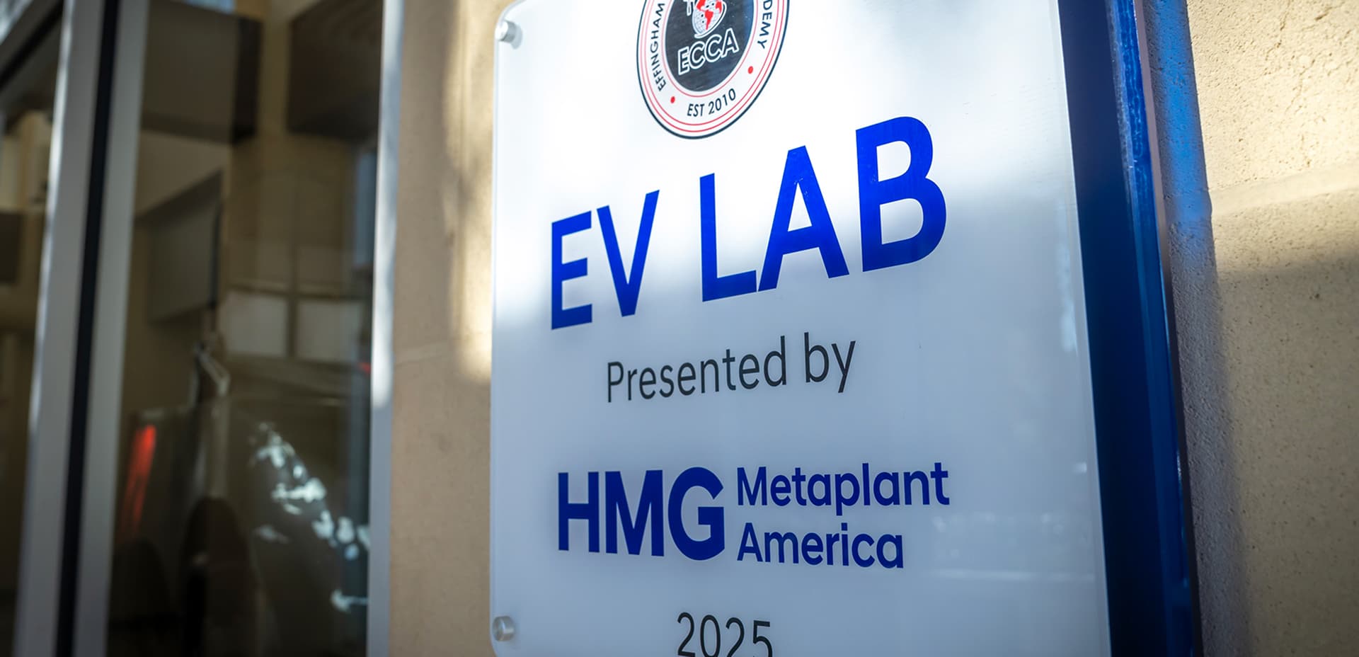 EV Lab presented by HMG Metaplant America signage mounted outside a school entrance, established 2025.