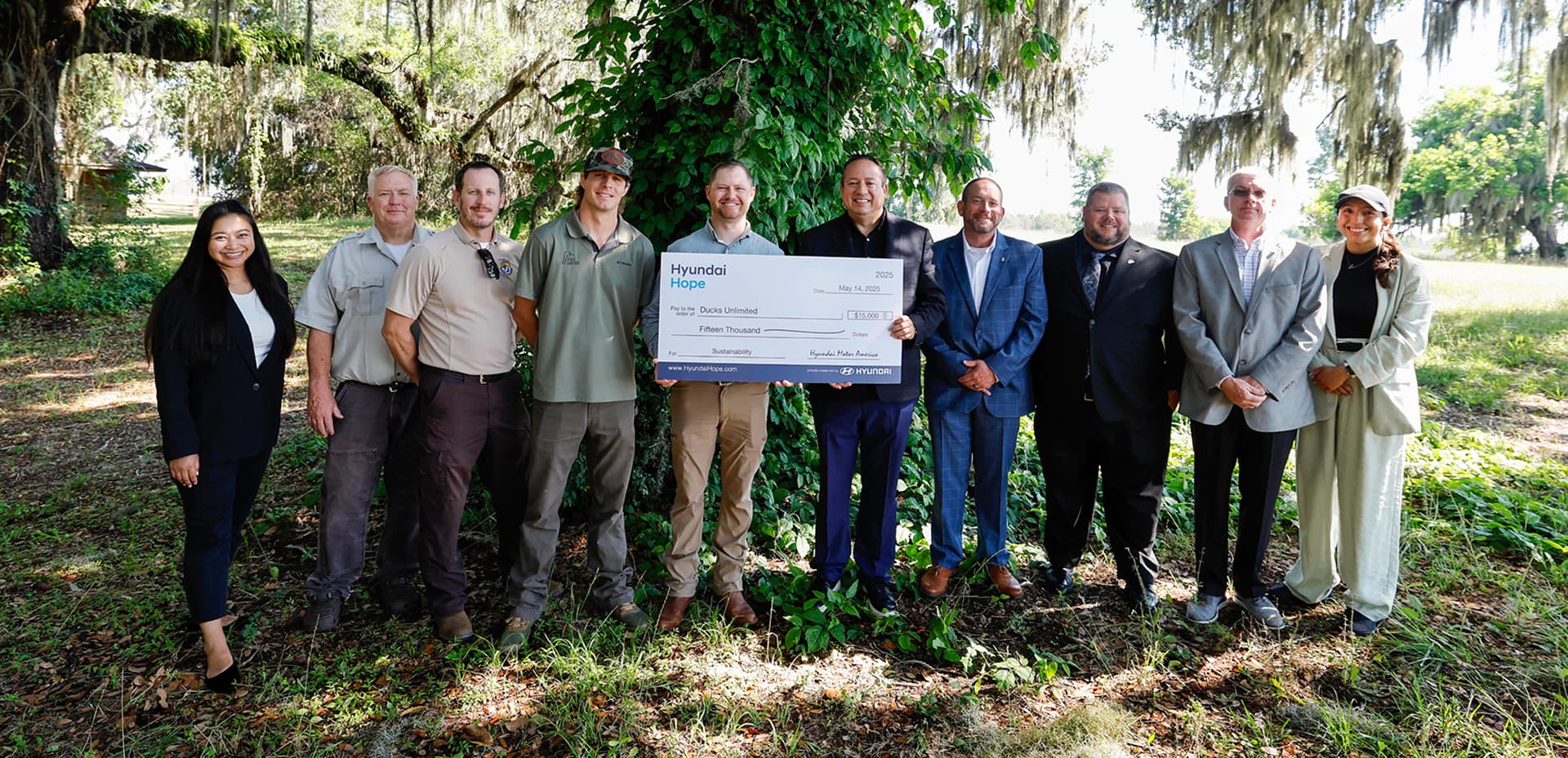 Group of Hyundai representatives and community partners posing outdoors with a ceremonial check made out to Ducks Unlimited for sustainability.