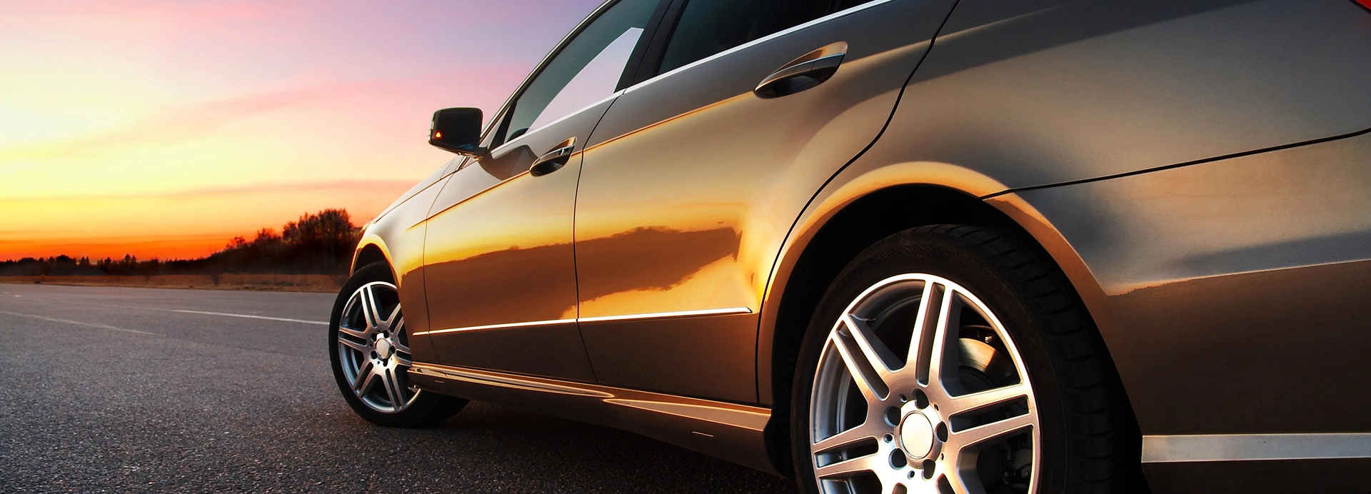 Side view of a car parked on the road with a sun set background.