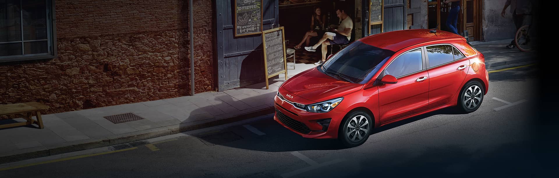 Red Kia parked on the side of a road