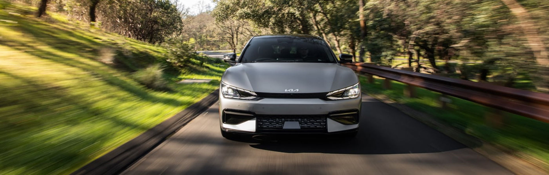Kia vehicle driving on road in wooded area