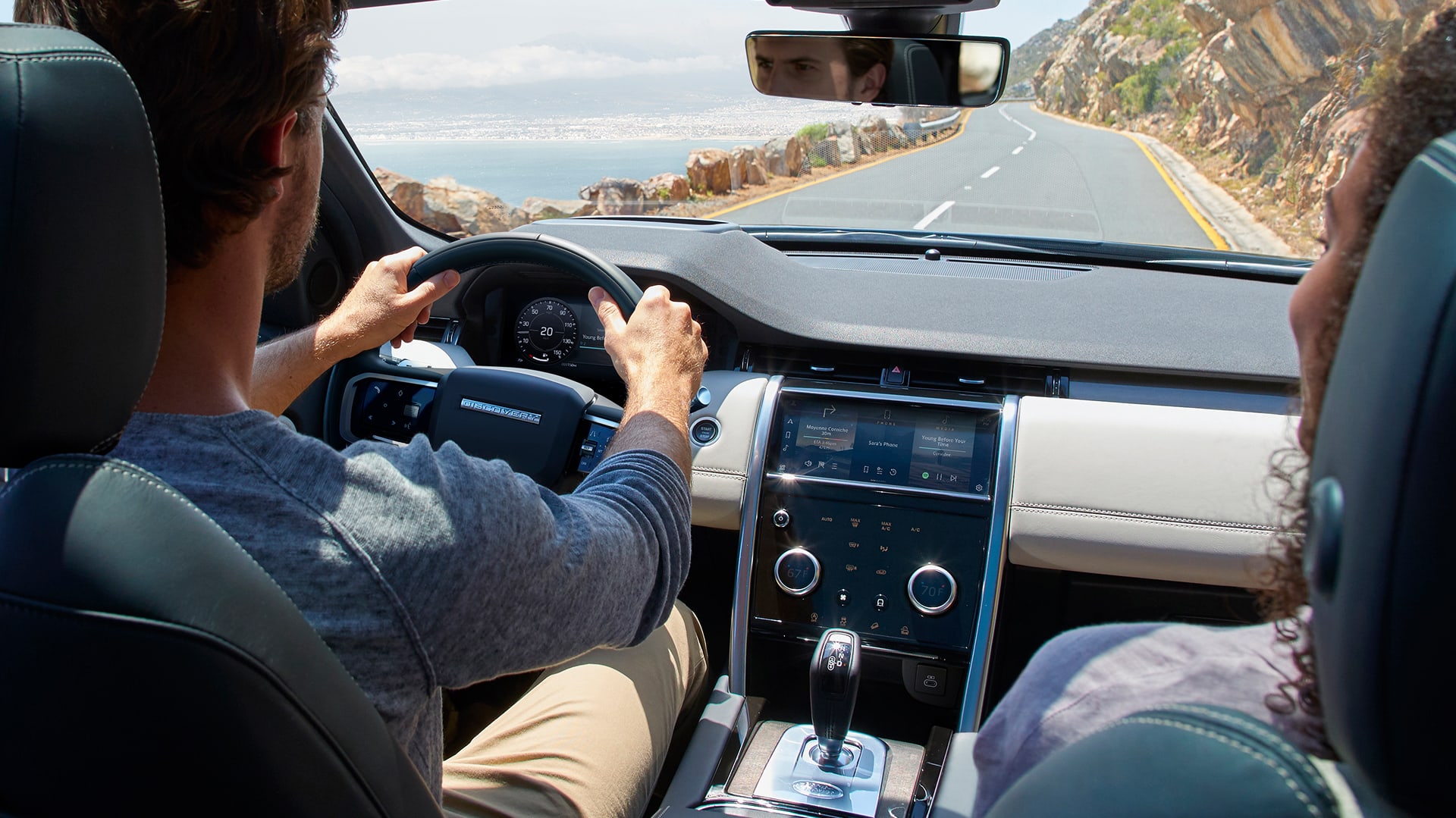 two people sitting on the inside of a Land Rover Discovery driving down a coastal road