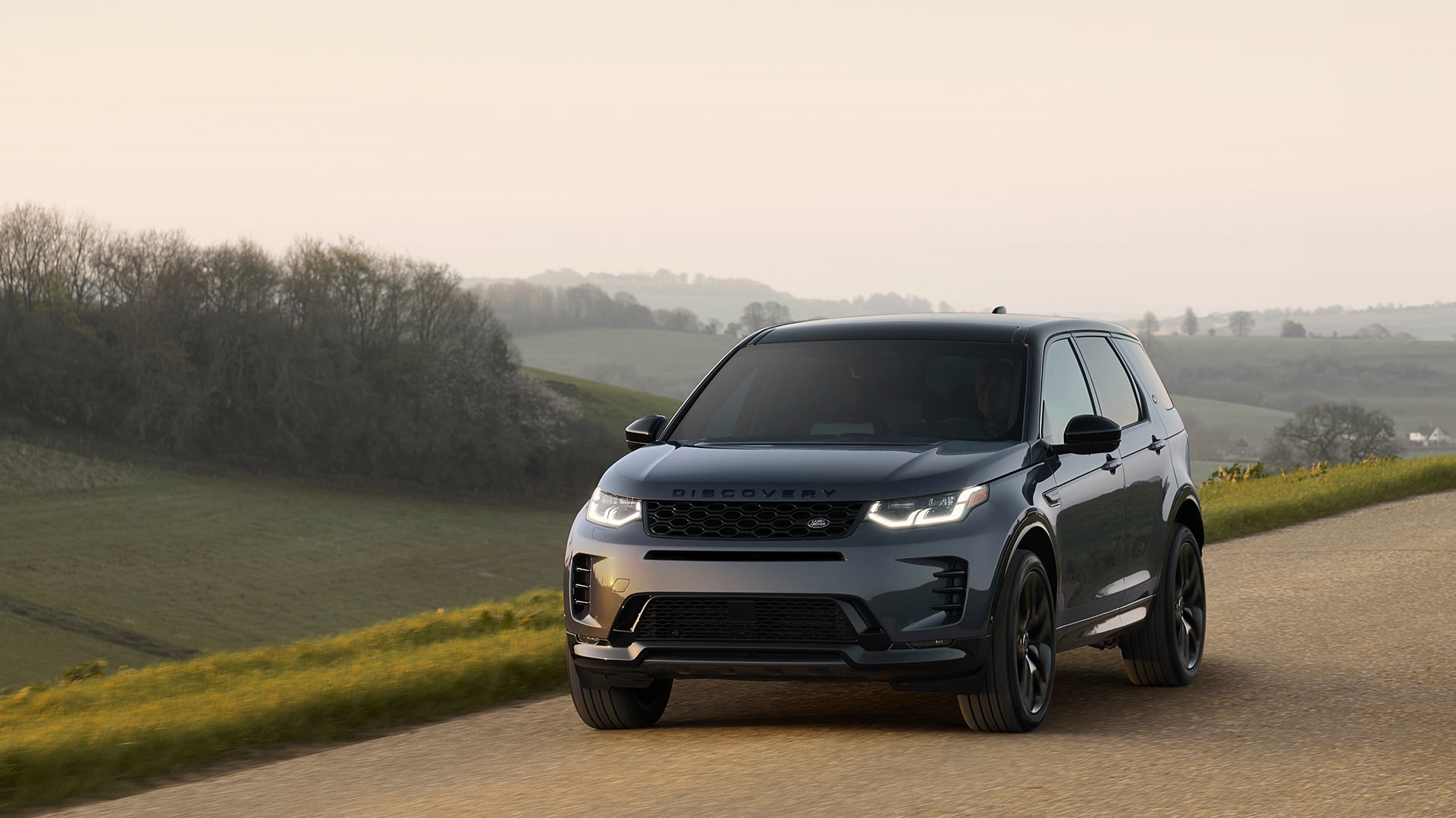 Front view of a Land Rover Discovery SUV driving outside on the road with grass and hills in background