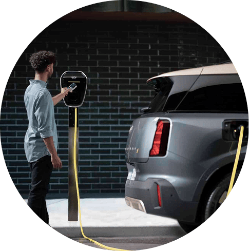 Side  -view of a person charging their MINI Countryman SE ALL4 against a brick wall.