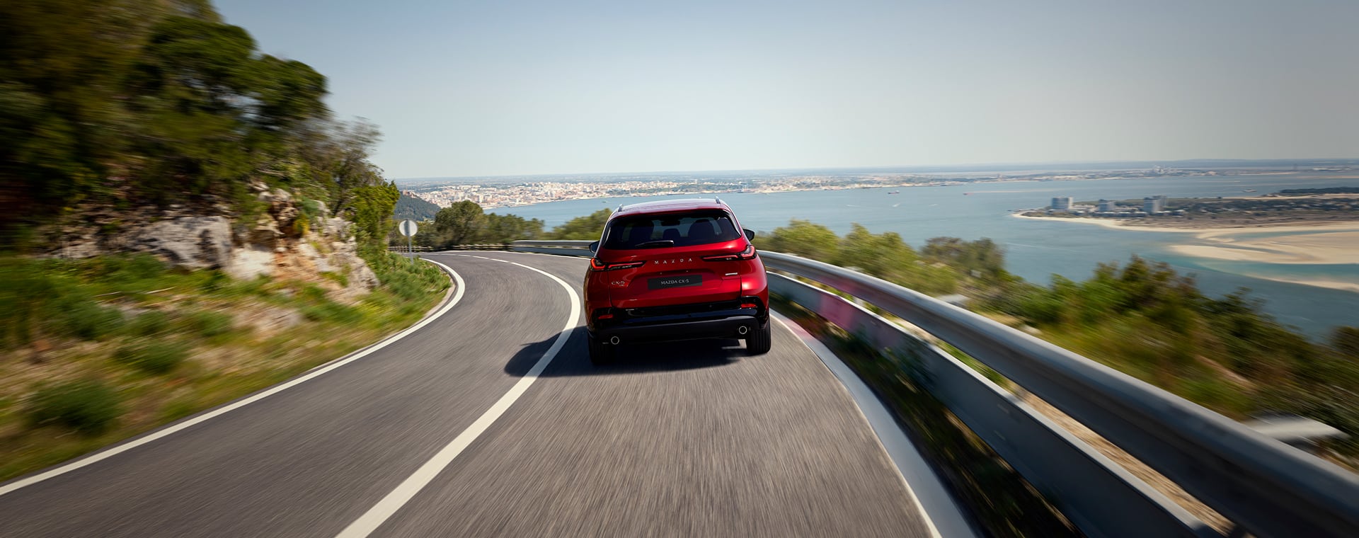 Red Mazda vehicles driving along coastline