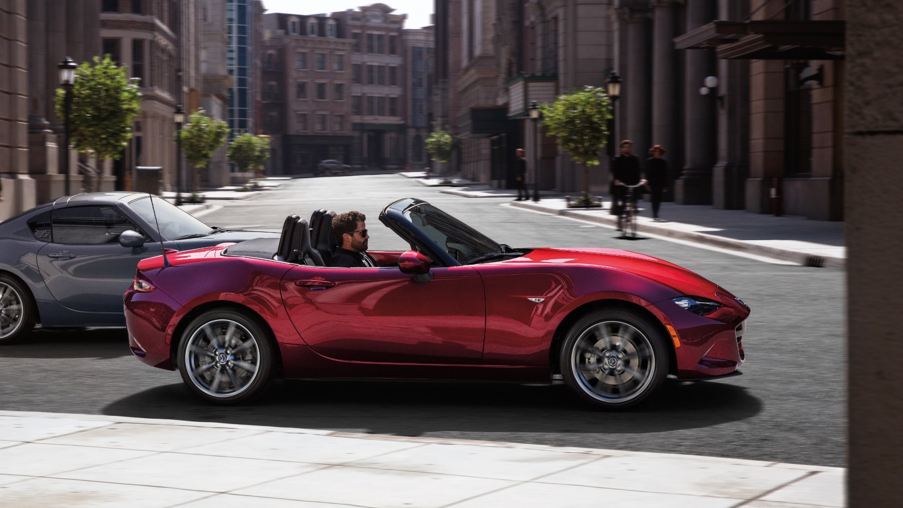 Two Mazda MX-5 Miatas driving in the city