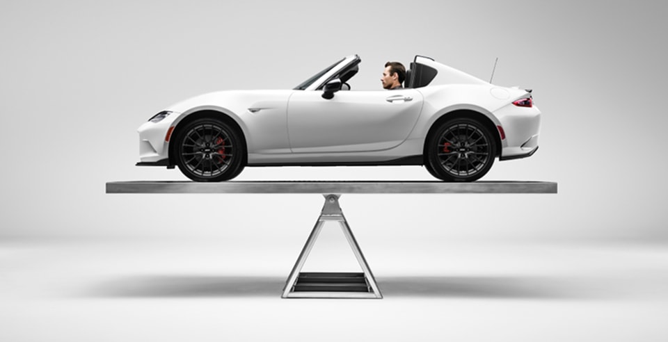 illustration of a 2026 Mazda MX-5 Miata RF balanced on a scale