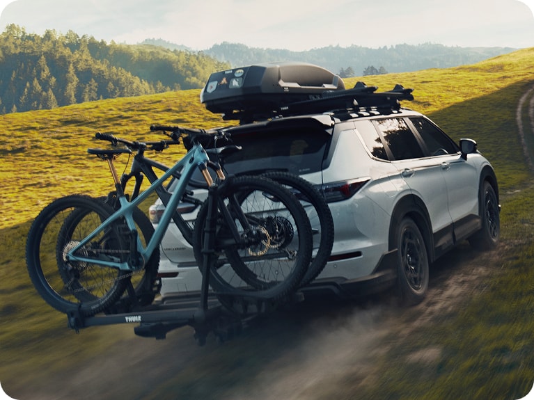 Back of White Mitsubishi Outlander Trail with bikes and roof rack