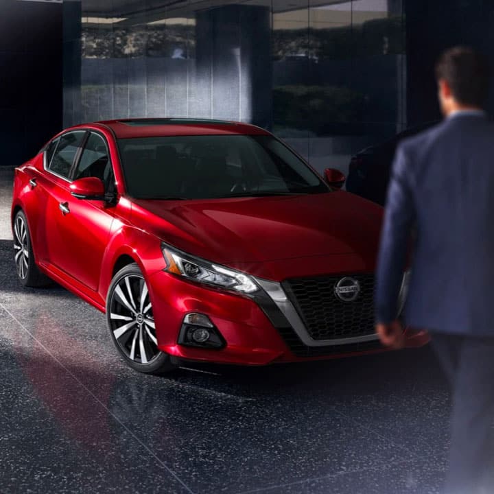 Man in suit walking toward red Nissan
