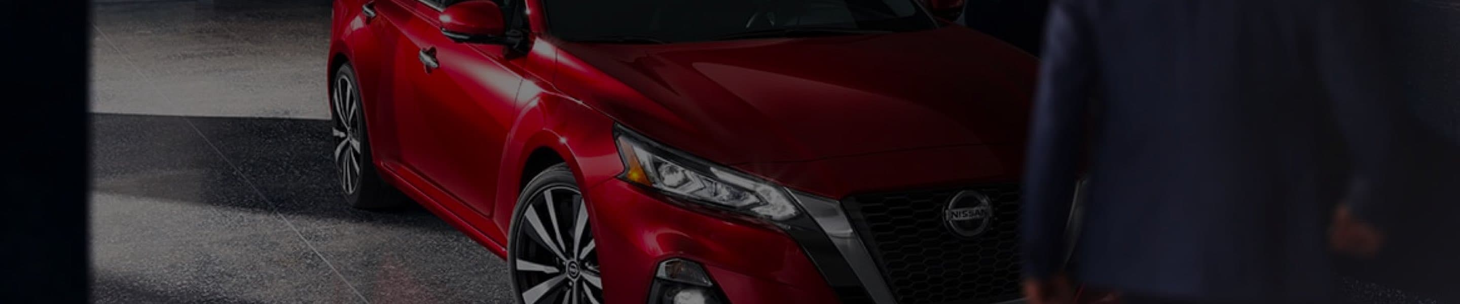 Red Nissan Altima driving through city at night