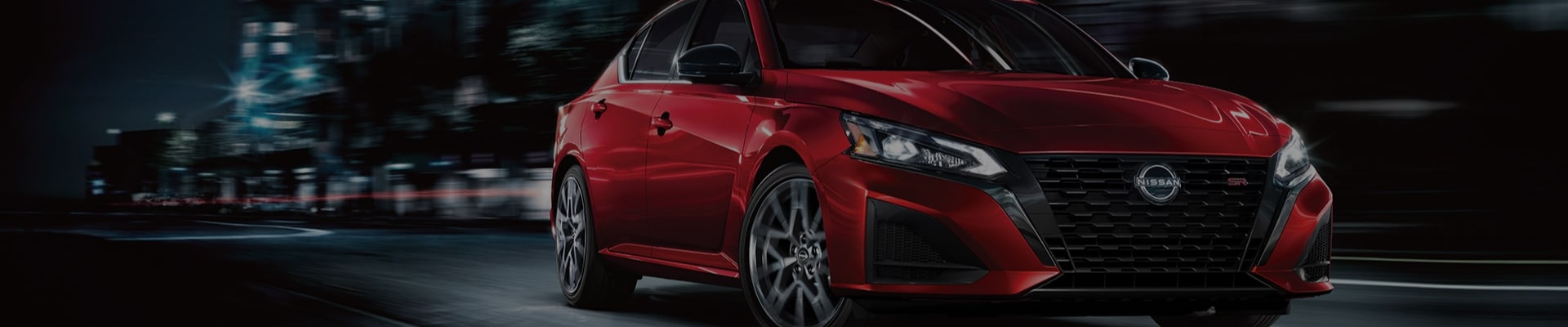 Red Nissan Altima driving through city at night