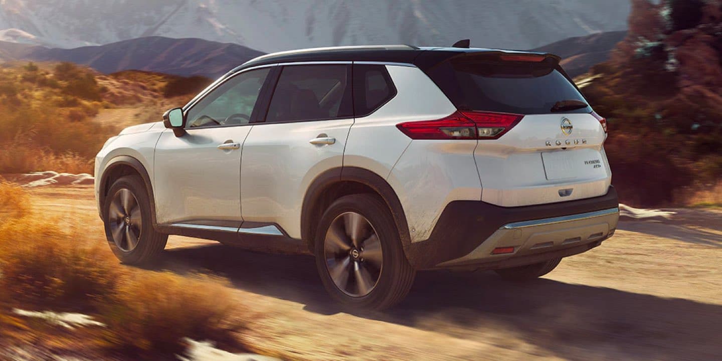 White Nissan Rogue driving on a dusty country road