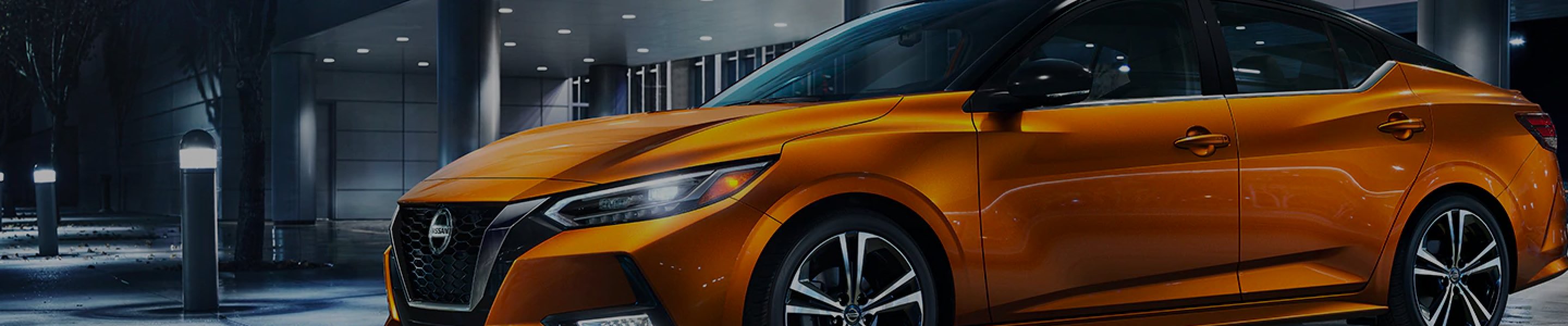 Orange Nissan Sentra driving through city at night