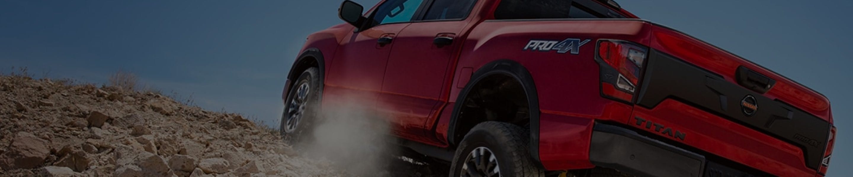 Red Nissan Titan driving up a rocky sandy hill
