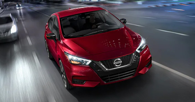Red Nissan Versa approaching viewer on road