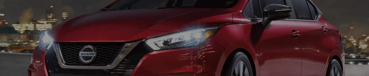 Red Nissan Versa driving through city at night