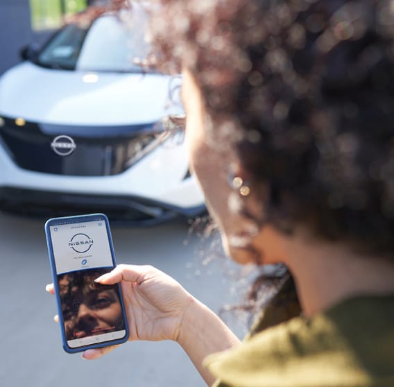 Woman holding phone towards Nissan vehicle.