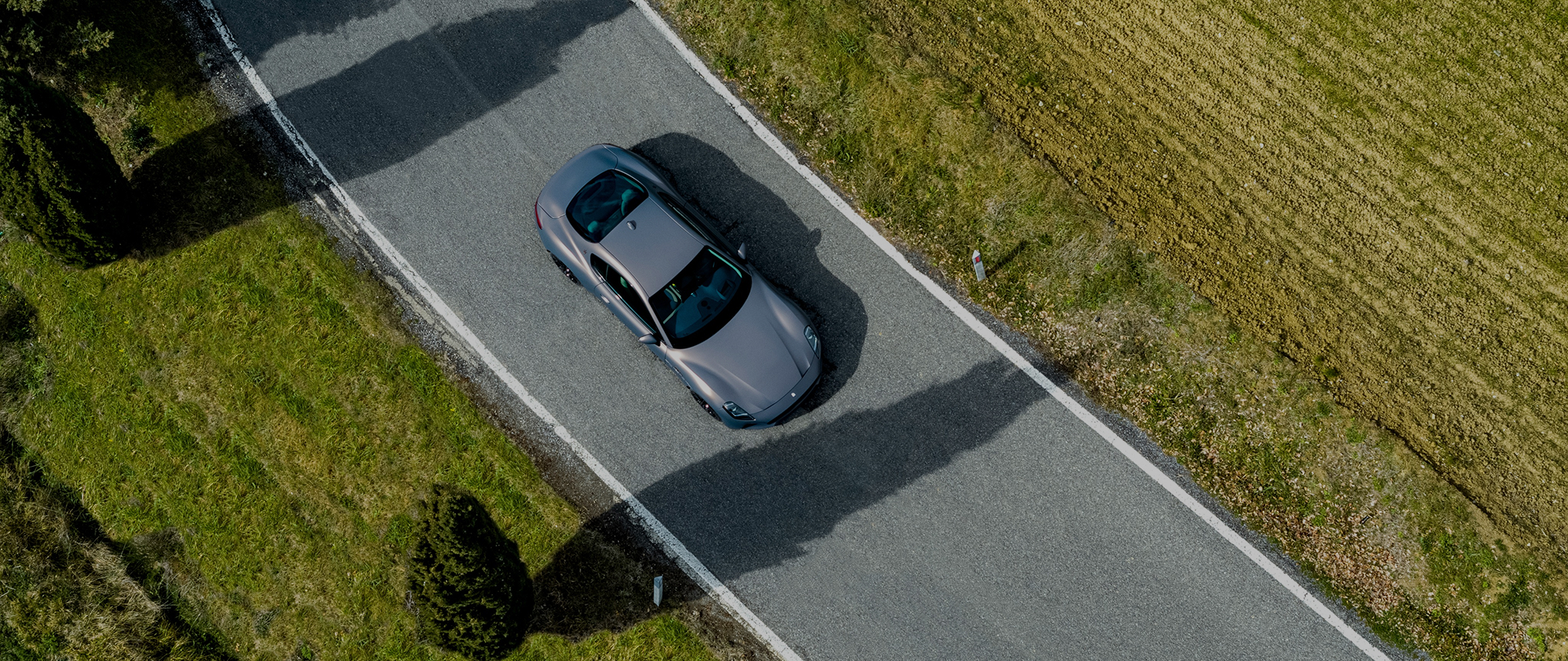 A silver car from over head driving on a road.