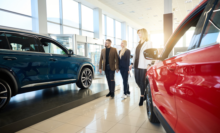 Three people standing between two cars in a dealership