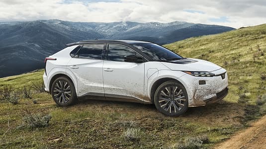 A static image of a white 2027 Subaru Solterra parked on a grassy hill. 