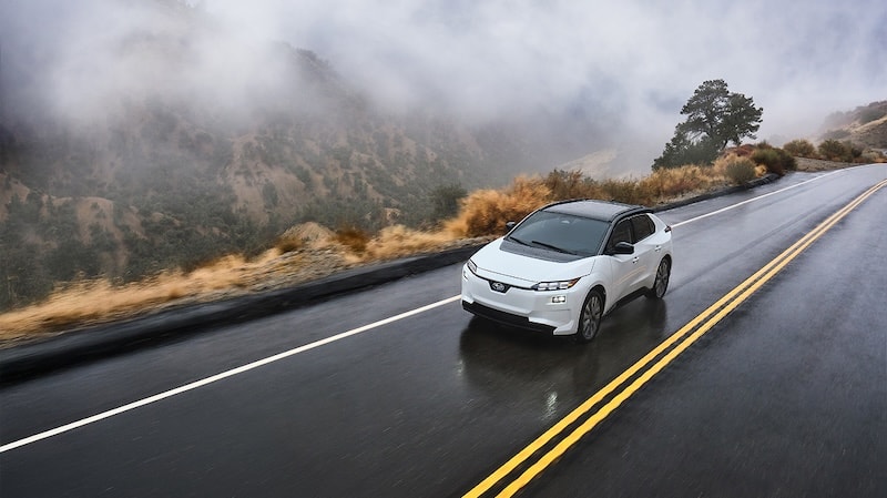 A Solterra AWD electric SUV drives on a narrow mountain road in the rain.