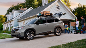 A family stands by a Subaru Forester with boxes and camping gear on its roof rack