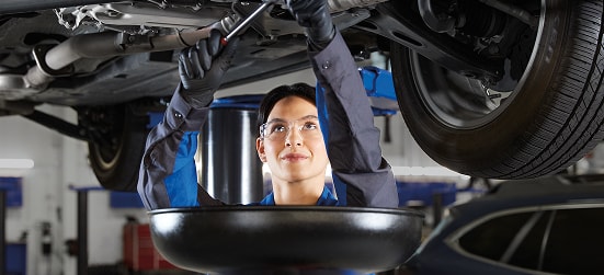 A Subaru service technician working under a vehicle on a lift