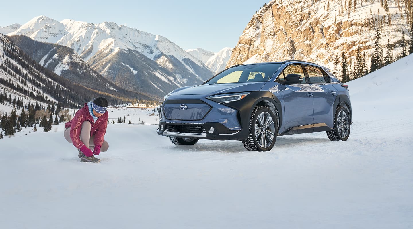 A static image of a blue 2026 Subaru Solterra parked on a snowy mountain landscape. 