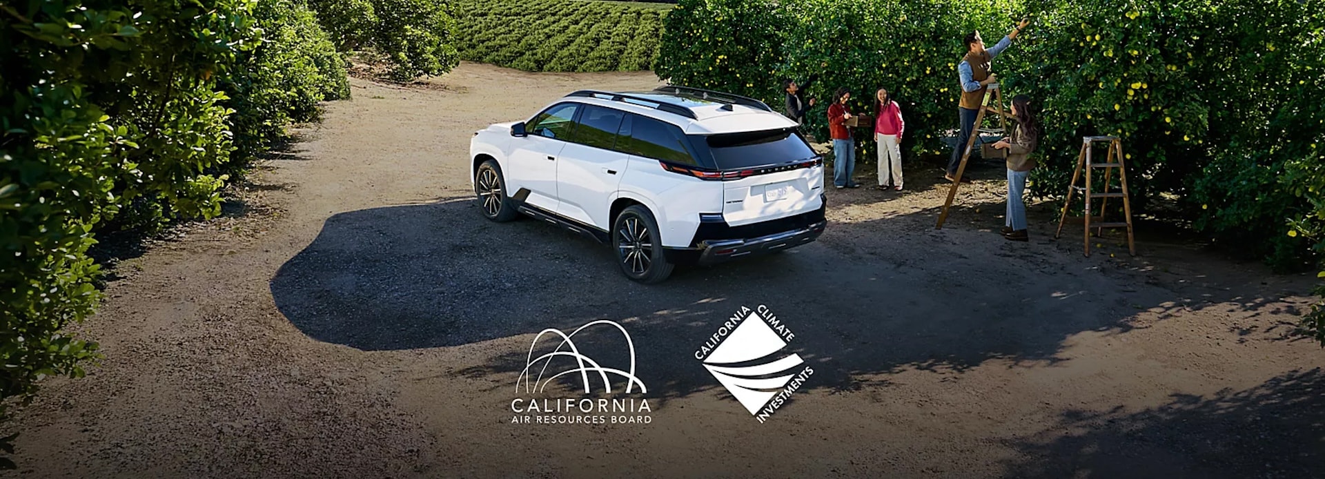 A white Subaru Getaway EV parked next to people picking fruit in an orchard.