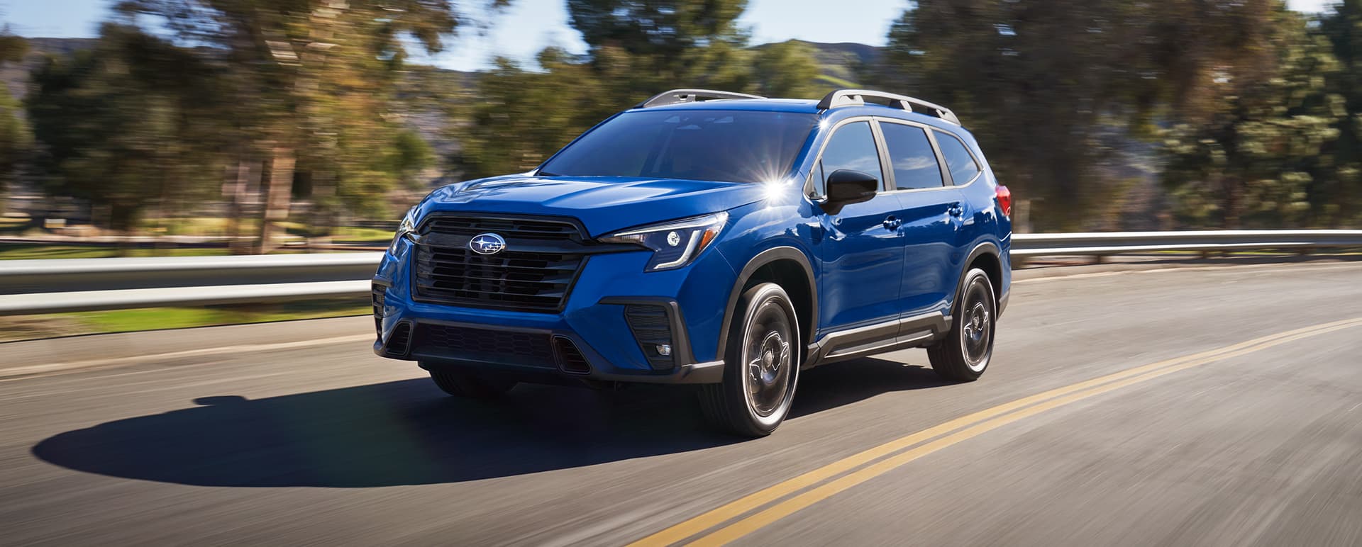 A blue Ascent 3-row SUV drives on a rural highway.