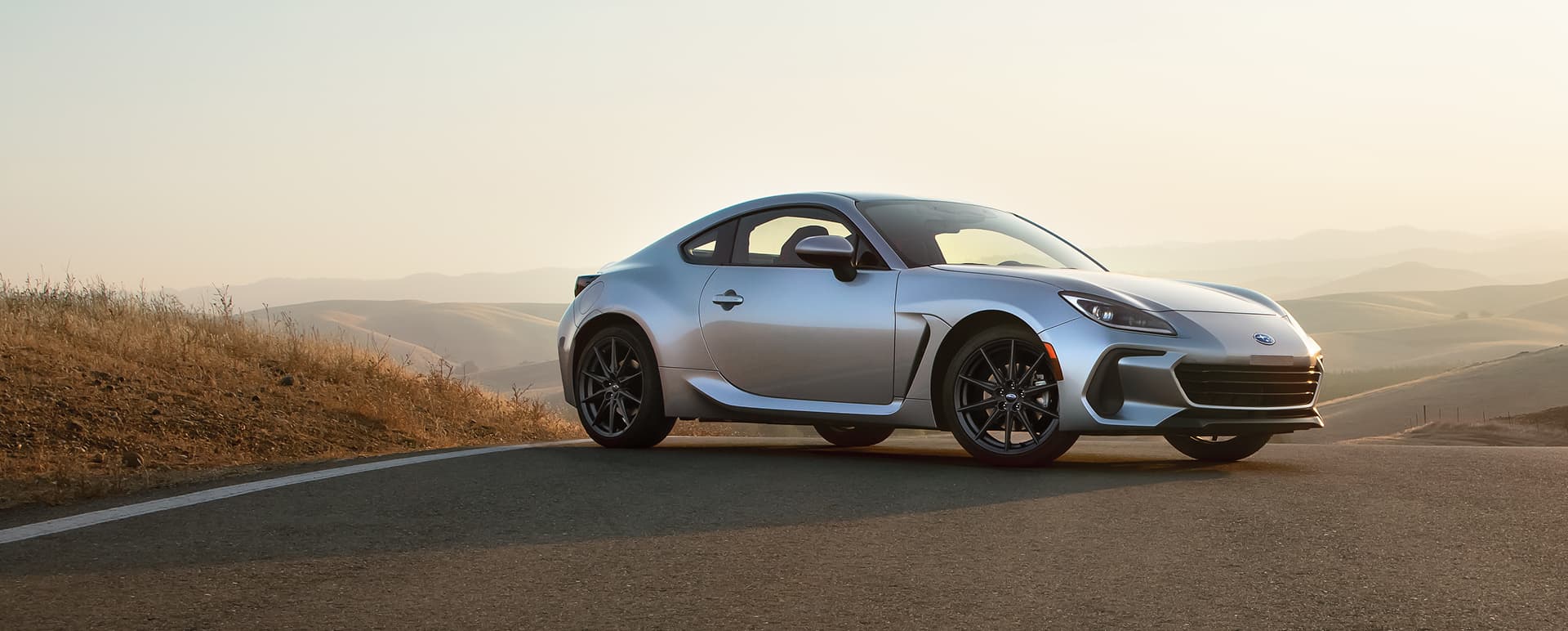 A silver BRZ parked on a road overlooking a hilly landscape.