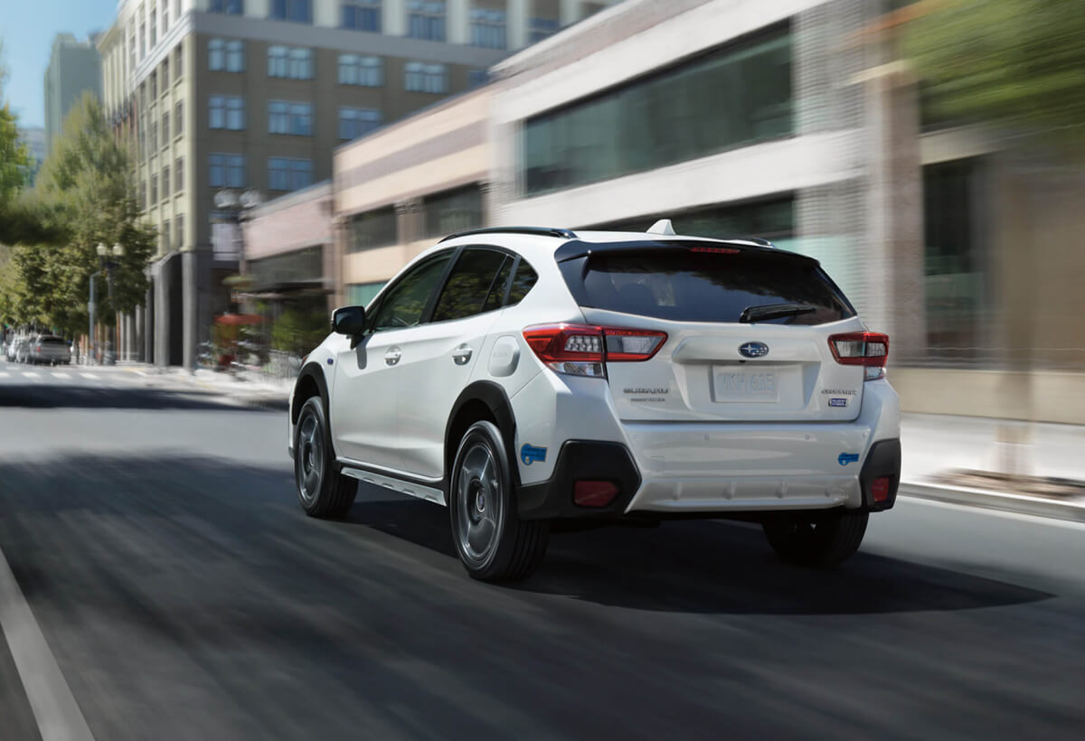 The rear corner of a white Subaru Crosstrek Hybrid driving on a street