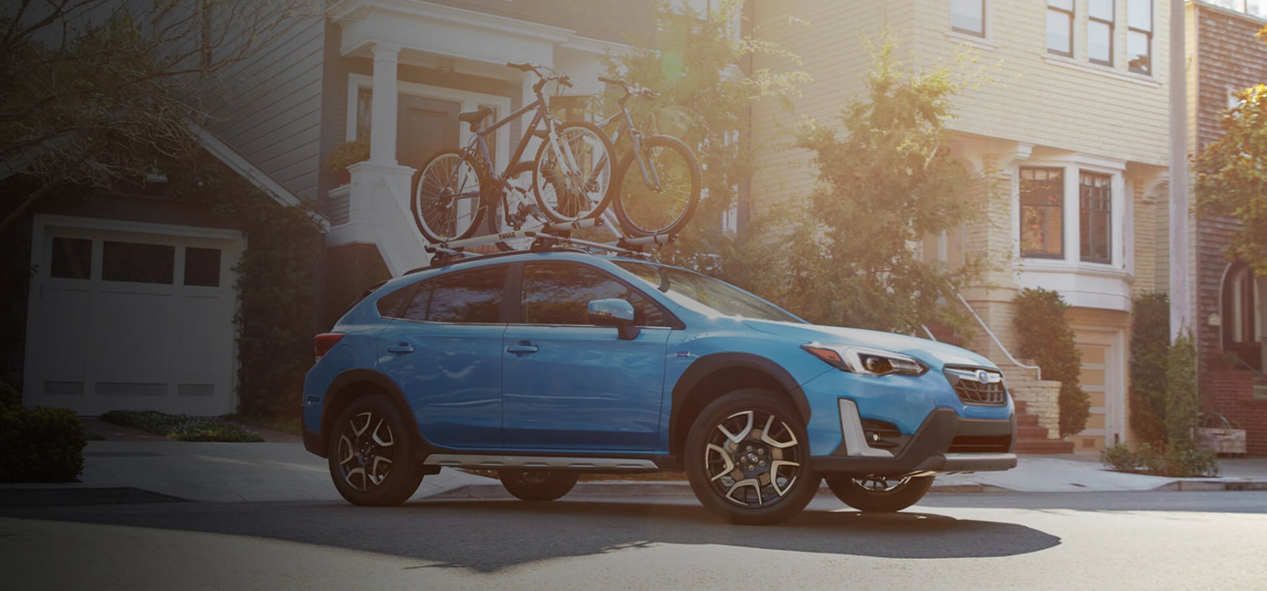 A blue Subaru Crosstrek Hybrid with two bicycles on its roof rack parked in front of a house