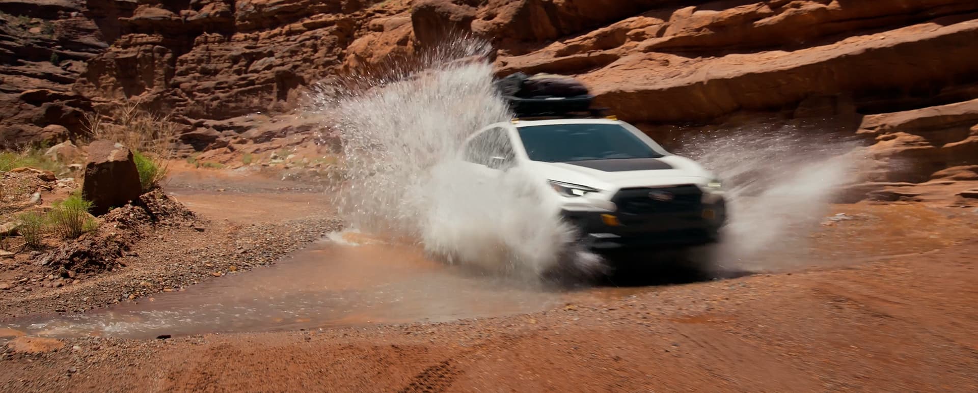 A 2027 Crosstrek Wilderness off-road compact SUV splashes through a puddle in a canyon. 
