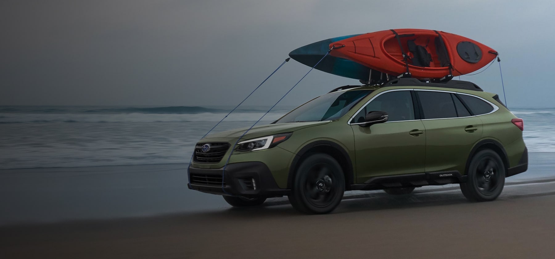 A 2022 Subaru Onyx Edition XT driving on a beach with kayaks mounted to its raised roof rails.