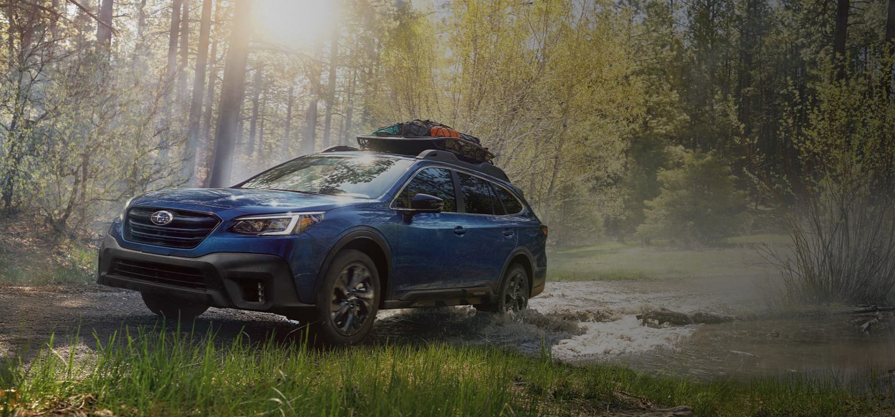 A 2022 Subaru Outback driving on a backcountry road with a cargo carrier on its standard raised roof rails.