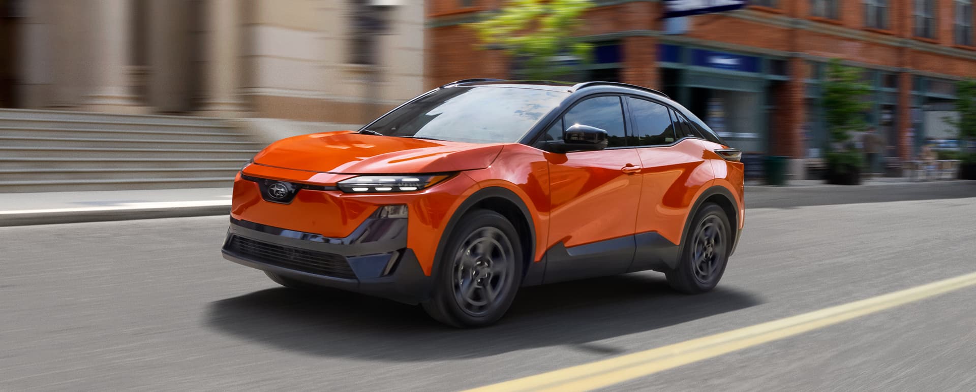 An orange Subaru Uncharted EV drives down a city street.