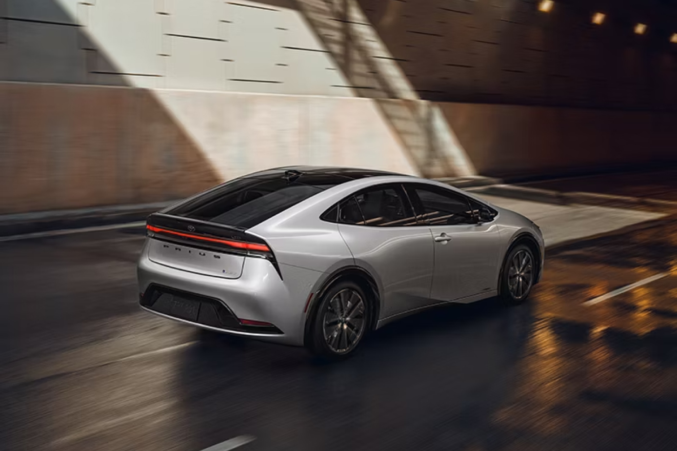 2027 Prius driving away on a road with a modern looking concrete backdrop