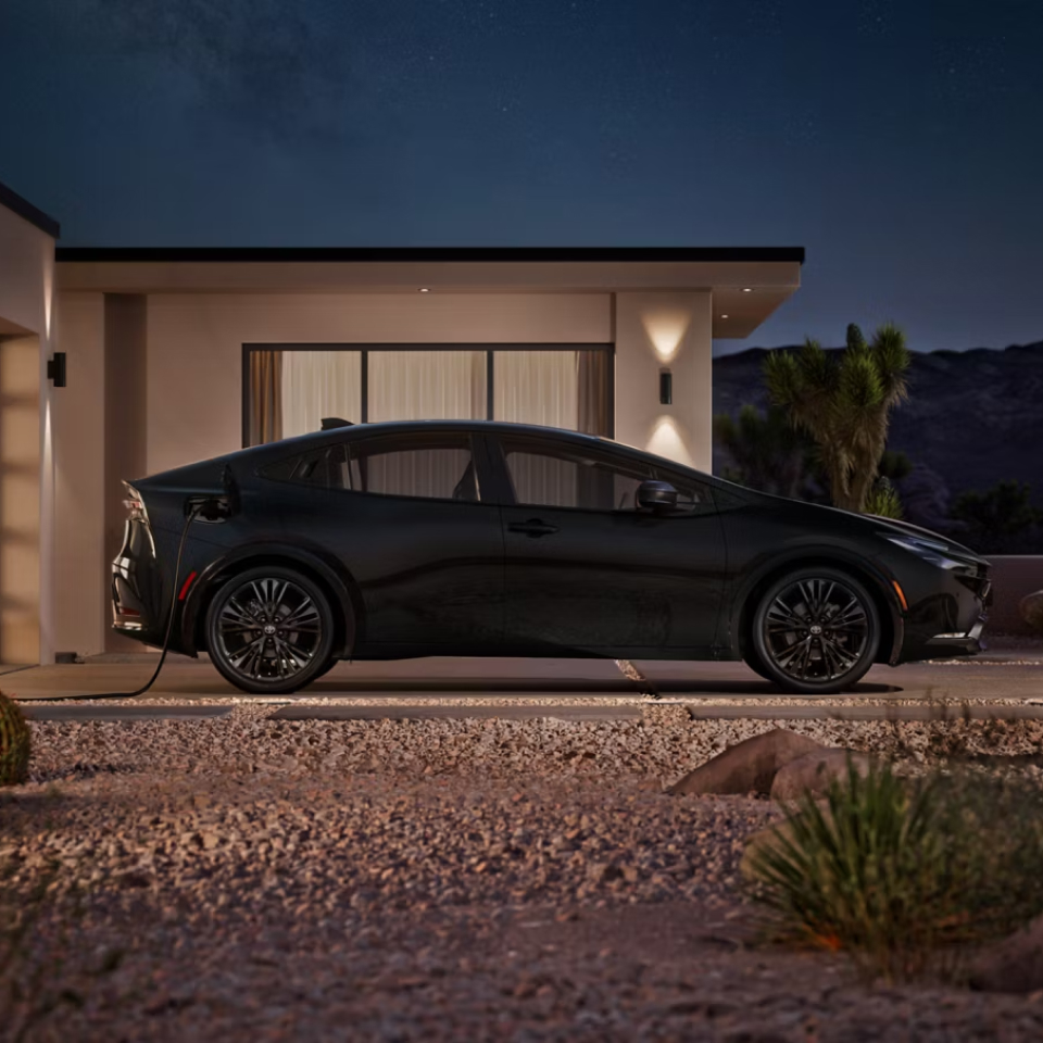 Side view of 2027 Prius Plug-in Hybrid parked in the driveway of a house at evening