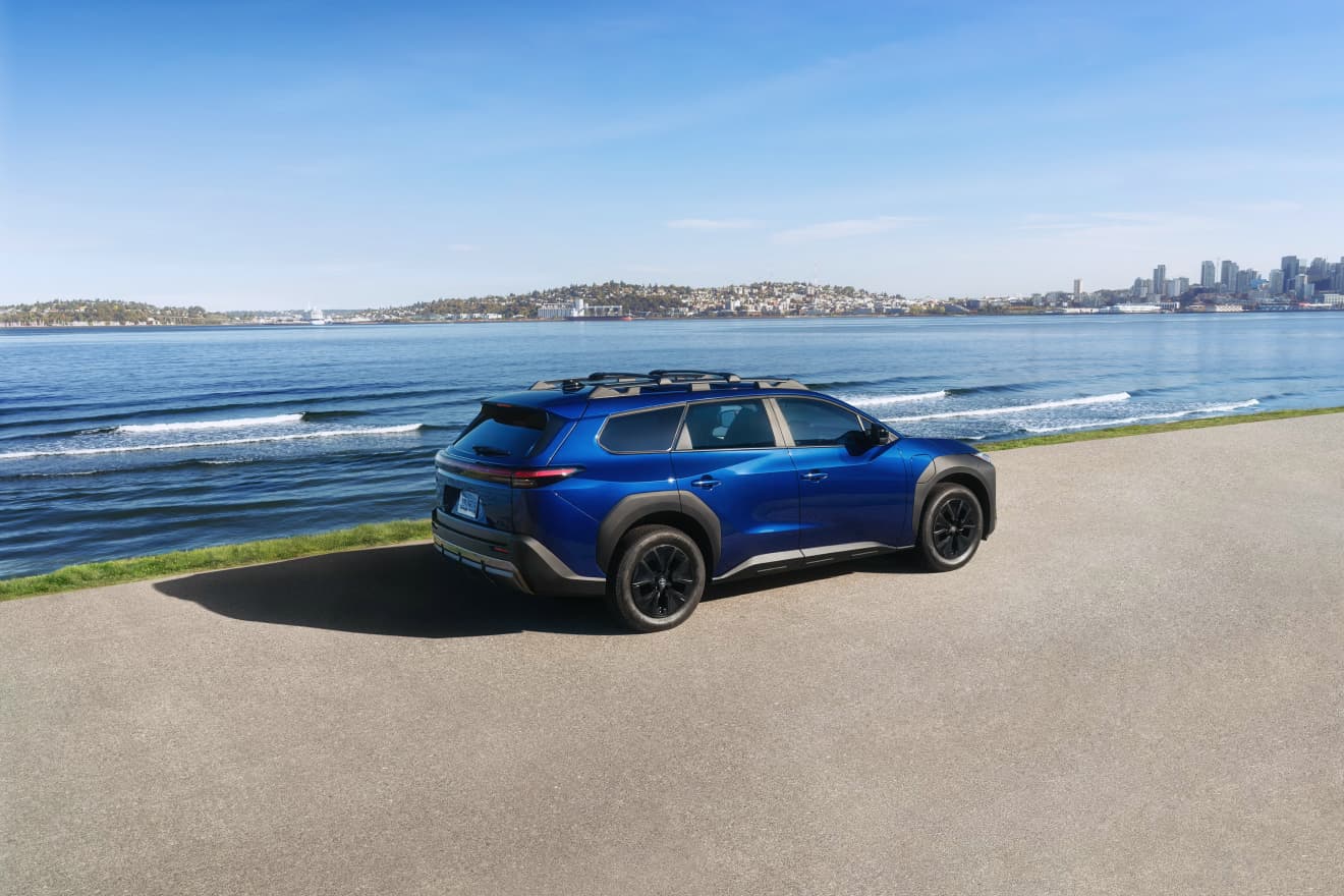 Blue 2027 Toyota bZ Woodland parked on a shoreline overlooking the water and city skyline