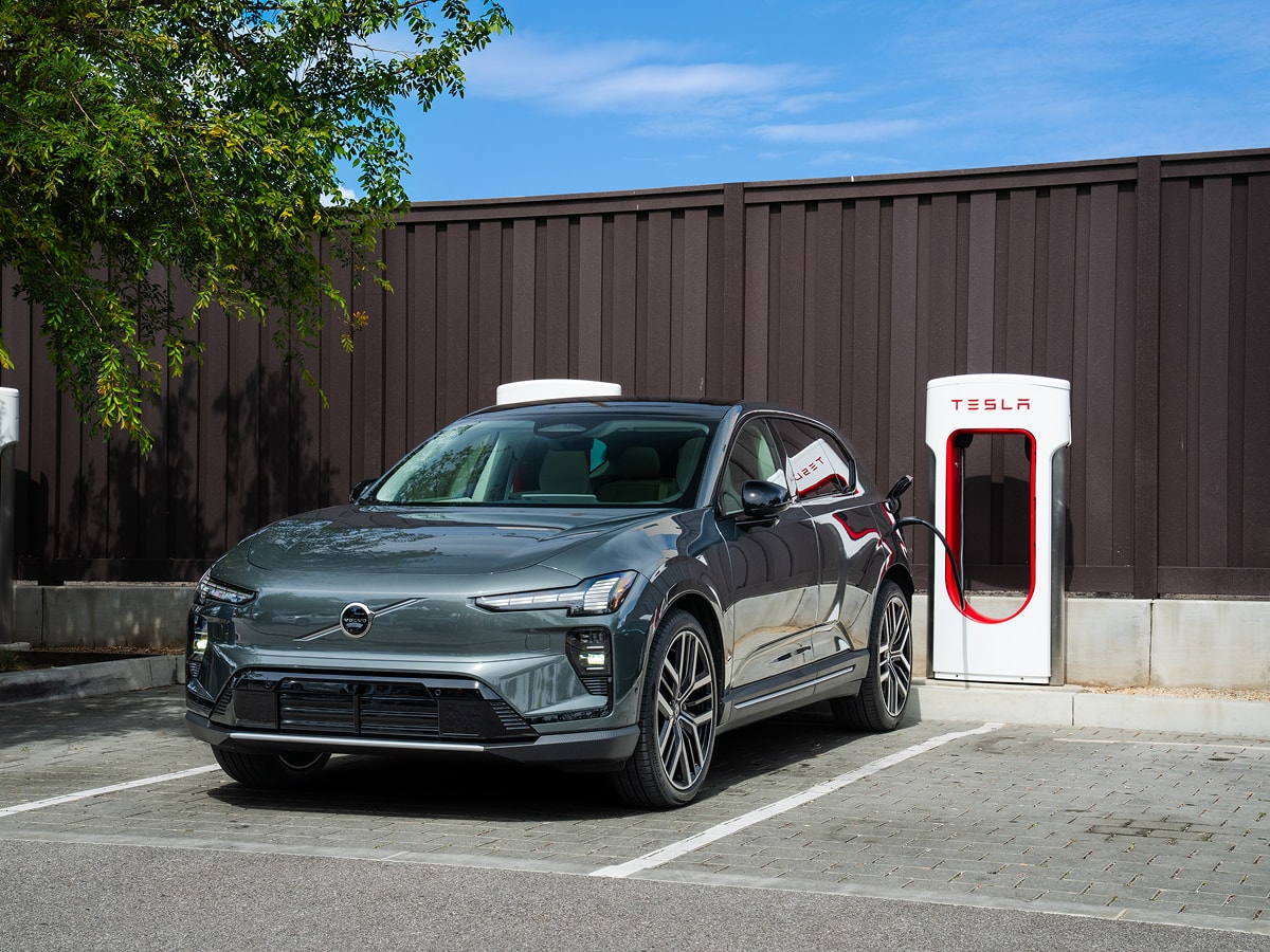 Green Volvo EX60 charging in a lot of Tesla Superchargers